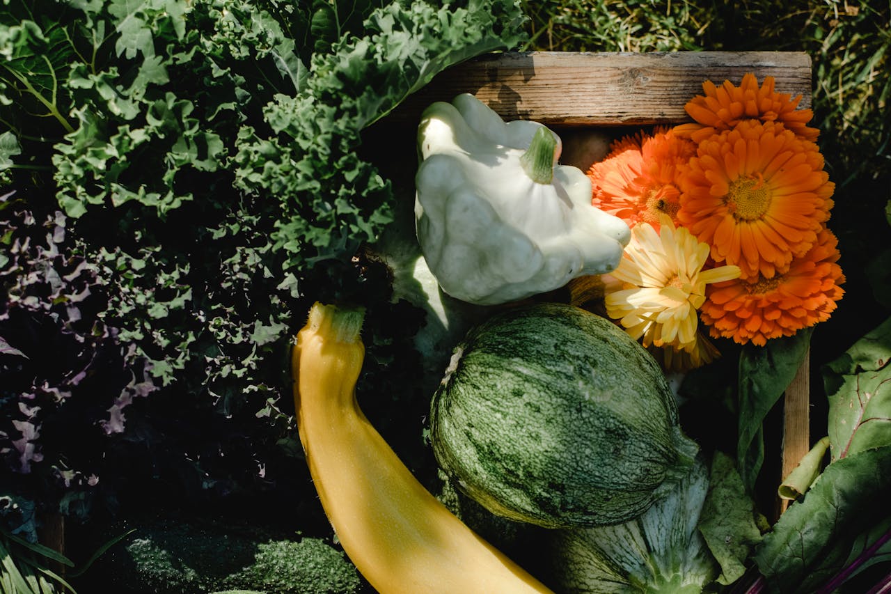 A vibrant collection of fresh garden vegetables and calendula flowers in a wooden crate, perfect for summer harvest.